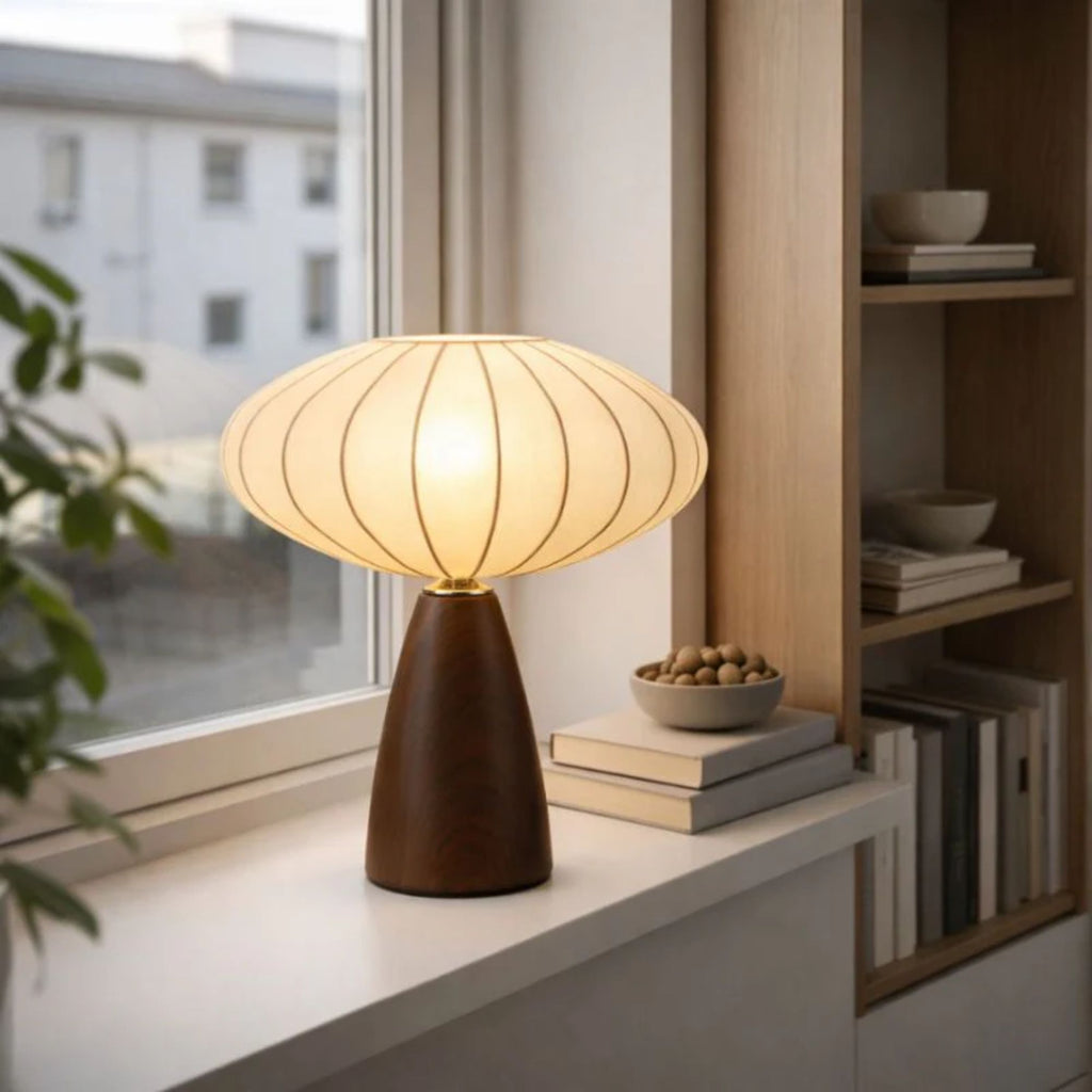 Modern bordslampa i trä med rund skärm placerad i fönster med varm belysning i skandinaviskt hem