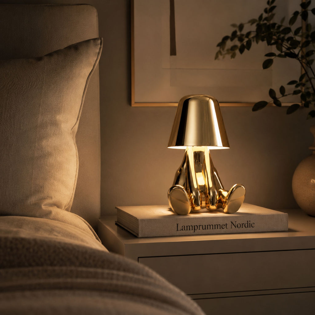 Uppladdningsbar bordslampa Buddy i guld som stämningsbelysning på ett nattduksbord.