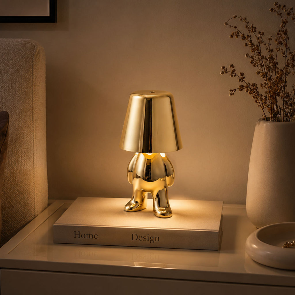 Uppladdningsbar bordslampa Buddy i guld som lyser på ett nattduksbord i sovrum.