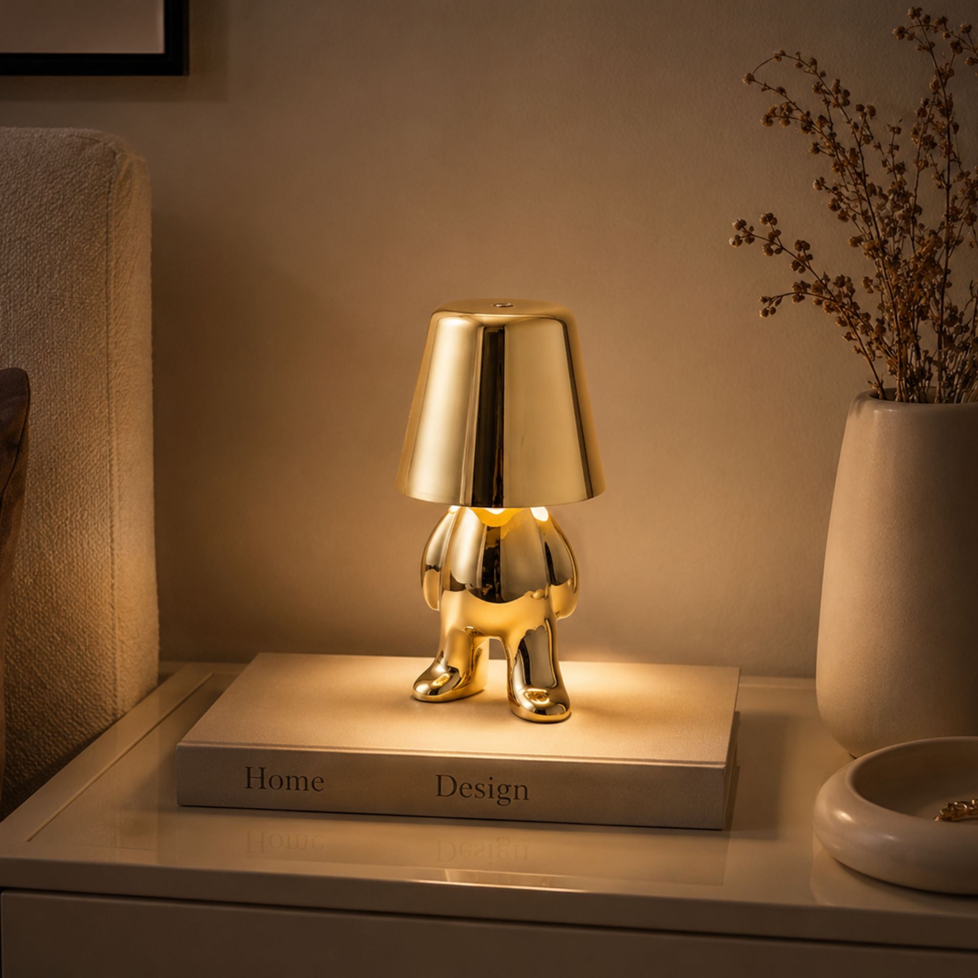 Uppladdningsbar bordslampa Buddy i guld som lyser på ett nattduksbord i sovrum.