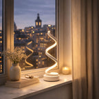 Bordslampa i modern vit design med LED-belysning placerad i fönster med utsikt över stad på kvällen.