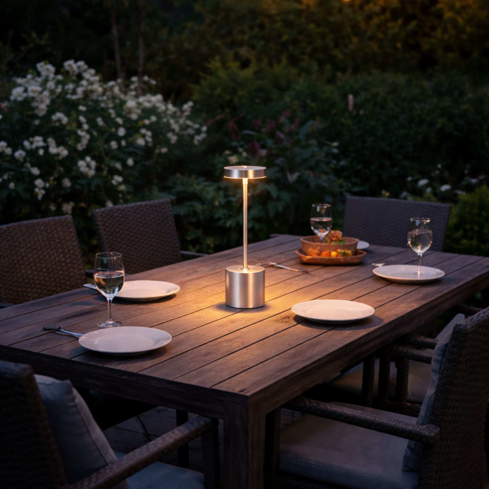 Bordslampa LED i silverfärgad metall på utebord som ger varm stämningsbelysning på terrass