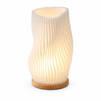 bordslampa med vågig design och integrerad LED som ger ett varmt mjukt ljus på vit bakgrund