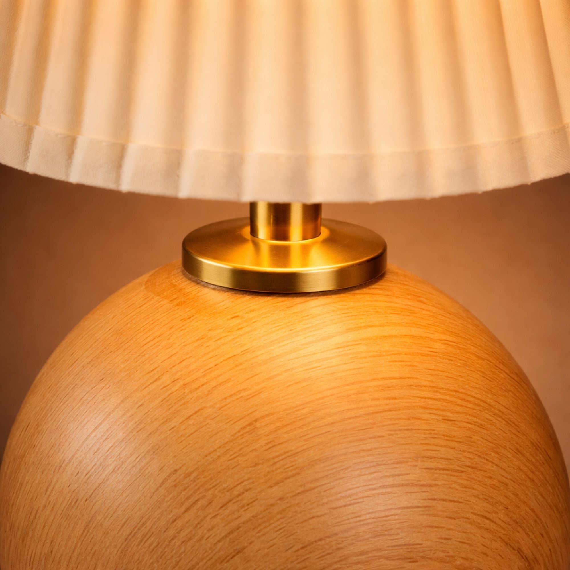 Närbild av bordslampa i ljust trä med guldfärgad detalj och plisserad lampskärm som visar hög kvalitet.