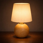 Bordslampa i ljust trä med plisserad lampskärm som ger varm och mysig LED-belysning.
