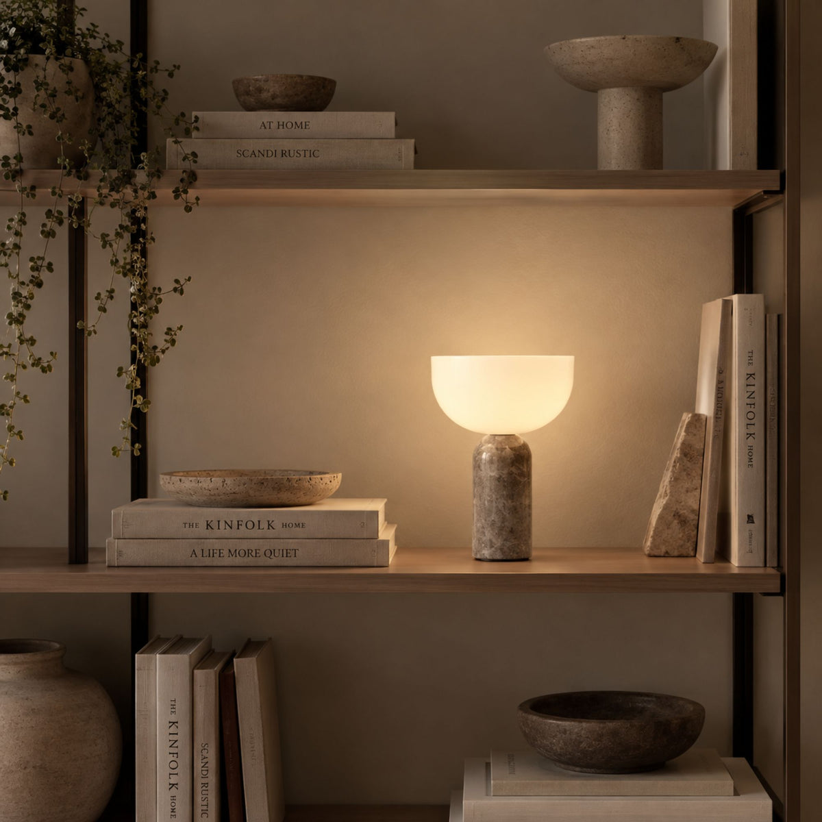 Bordslampa KINZO med grå marmorfot och varm belysning i bokhylla.