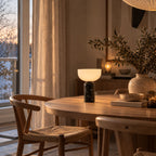 Bordslampa med svart marmorfot och vit skärm på matbord i trä.