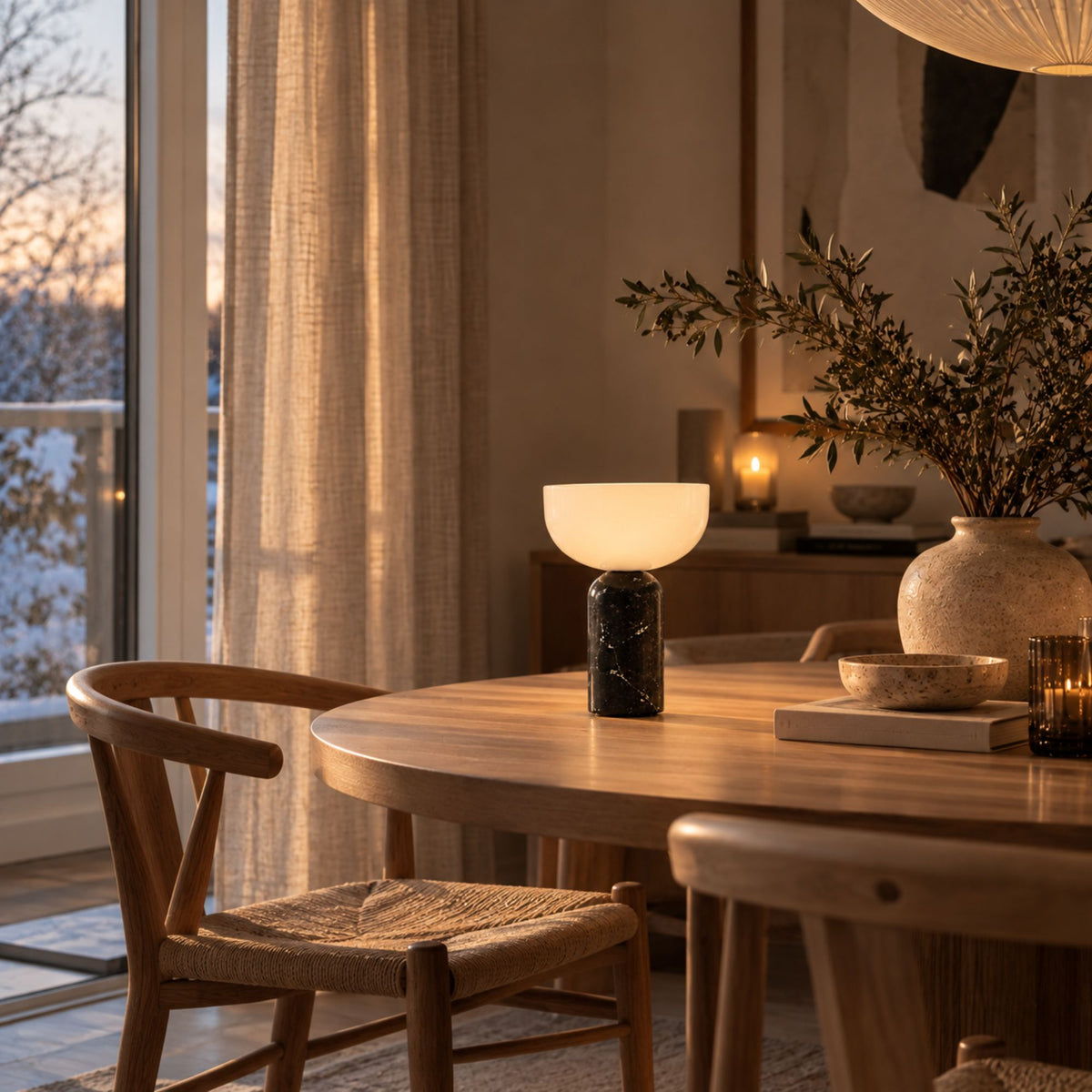 Bordslampa med svart marmorfot och vit skärm på matbord i trä.