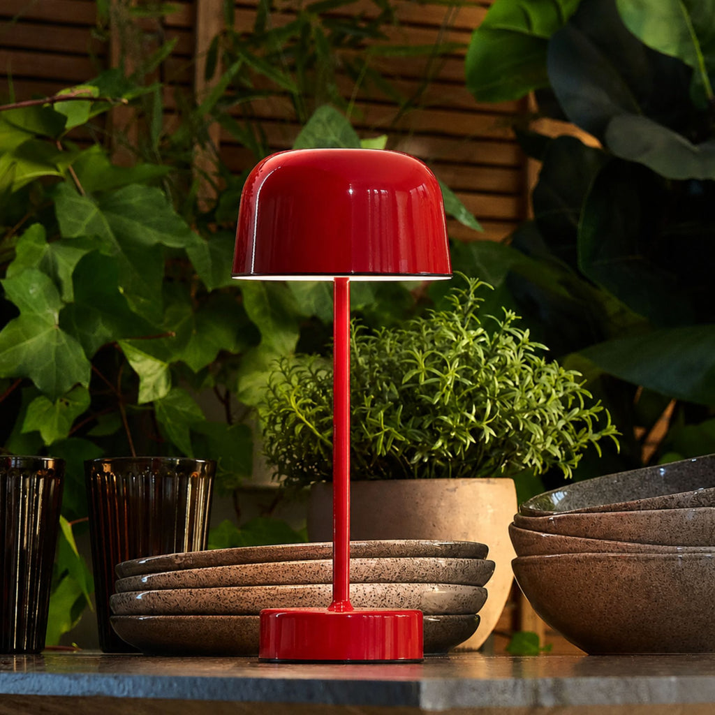 Röd uppladdningsbar bordslampa Domo på matbord med växter och varm stämningsbelysning.