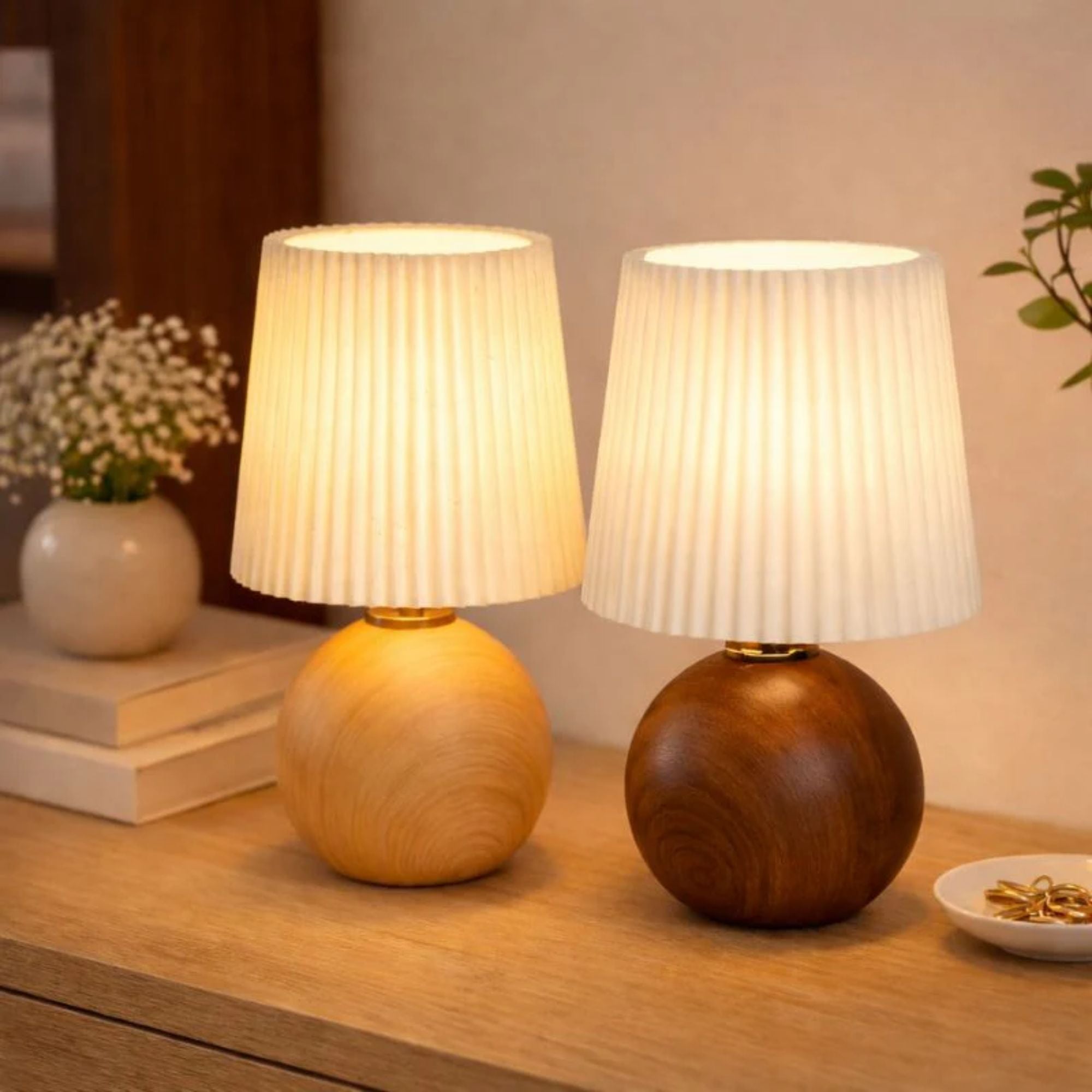 Två bordslampor i trä i olika färger med plisserad lampskärm och varm LED-belysning.