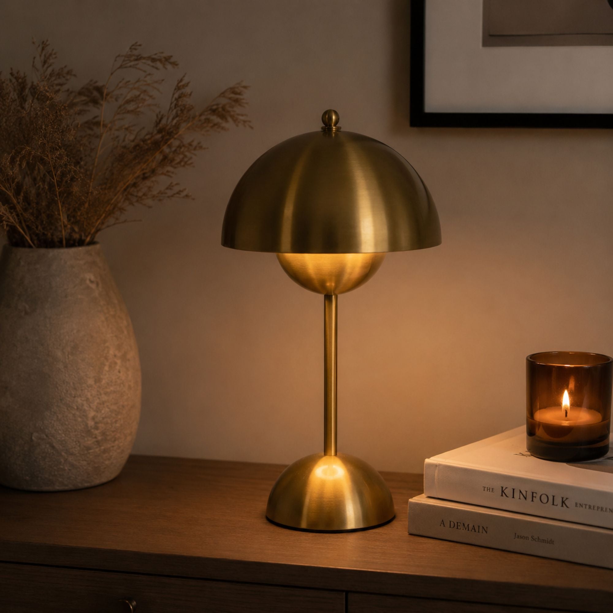 Portabel bordslampa i guld med varm stämningsbelysning på ett sideboard tillsammans med ljus och keramik.