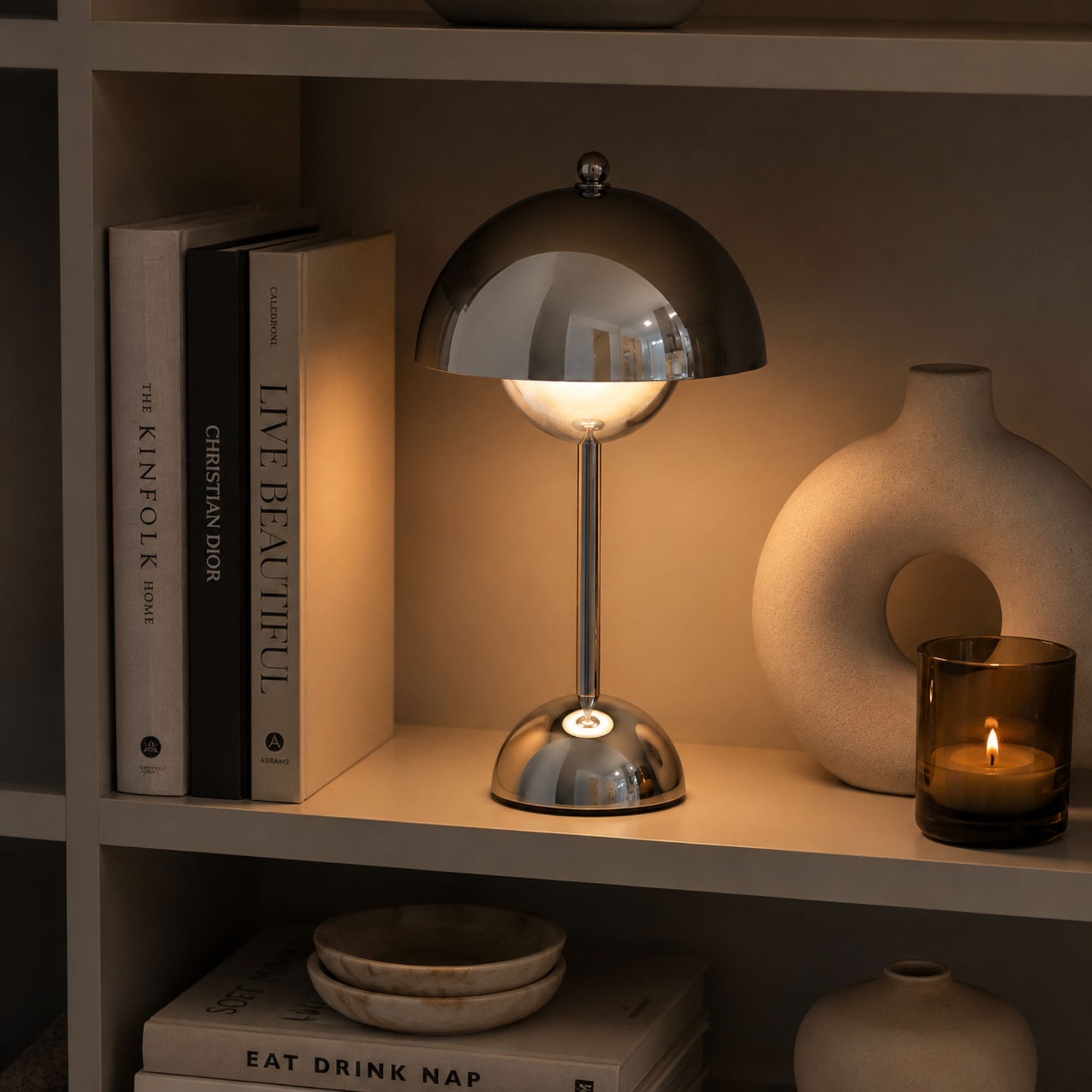 Flowerbud bordslampa i krom placerad i en stilren bokhylla i skandinaviskt hem.