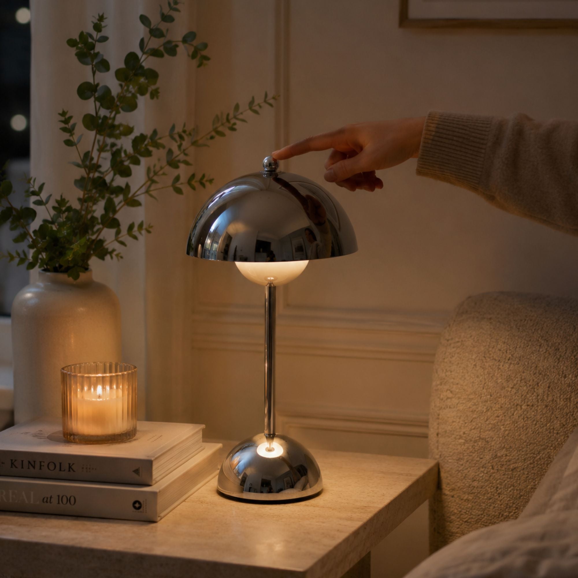 Hand som tänder Flowerbud bordslampa i krom med touchdimmer på ovansidan.