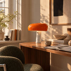 Orange bordslampa med marmorfot på ett skrivbord i trä med böcker och stilren inredning.