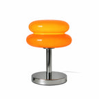 Orange retro bordslampa i glas med kromfot på vit bakgrund