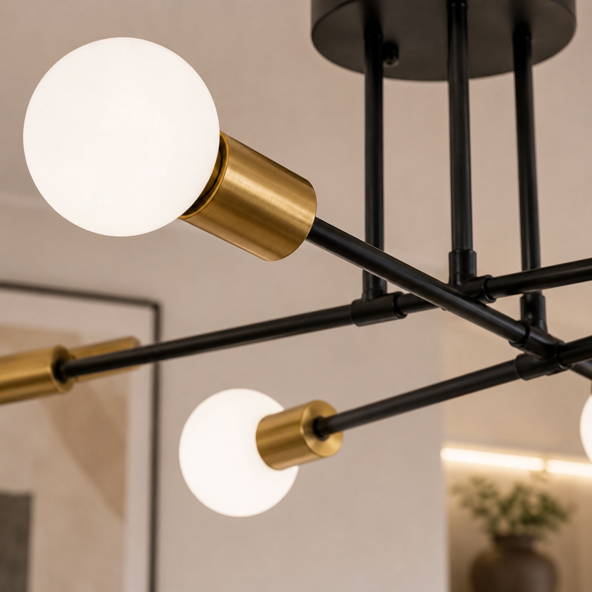 Taklampa detaljbild i close-up som visar svartlackerad metall, guldfärgade lamphållare och vit glob i frostat glas med modern exklusiv design och varm elegant belysning.