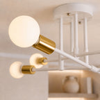 Taklampa detaljbild i close-up som visar vitlackerad metall, guldfärgade lamphållare och vit glob i frostat glas med modern exklusiv design och mjuk varm belysning.