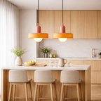 två taklampor i orange och rosa design hängande över köksö i modernt skandinaviskt kök med stilren och varm belysning