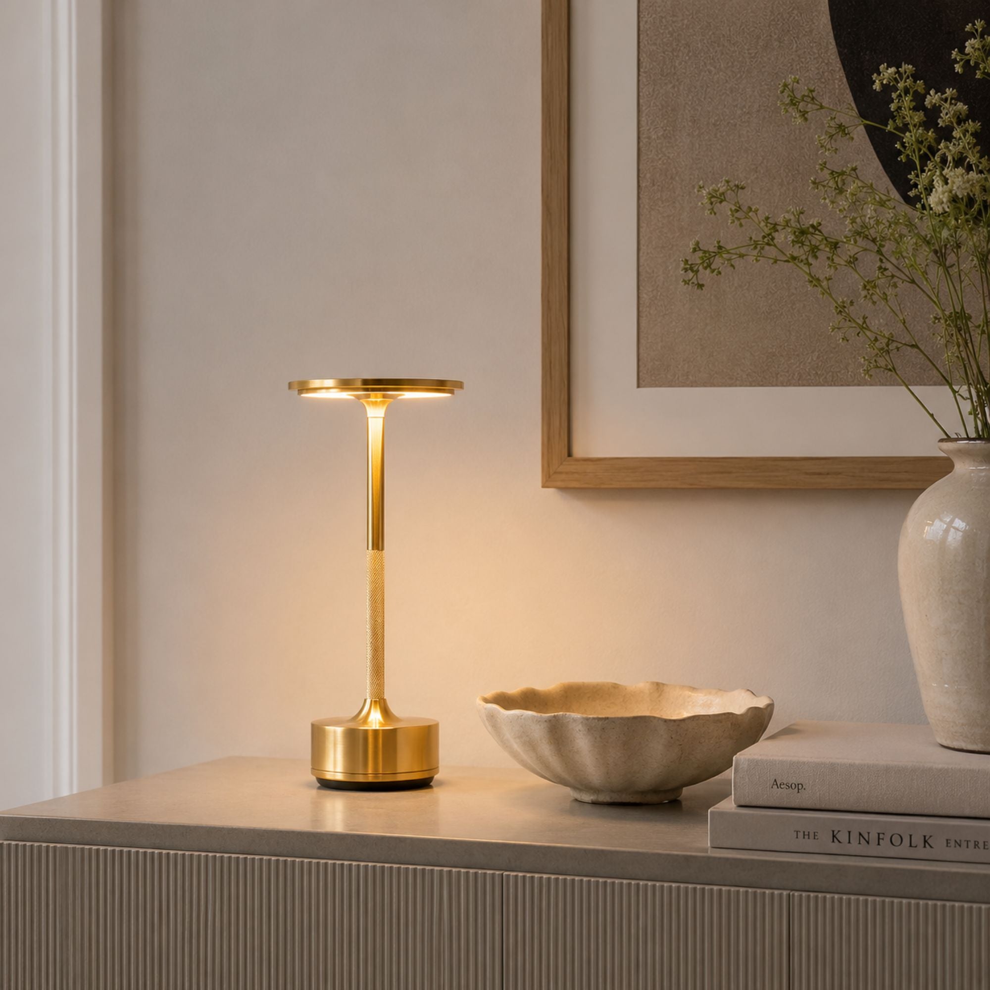 Uppladdningsbar LED-bordslampa i borstad guldfinish på skänk i modern skandinavisk inredning.