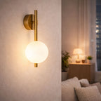 Modern vägglampa i guld med vit glaskupa som lyser i ett mysigt vardagsrum på kvällen med varm stämningsbelysning